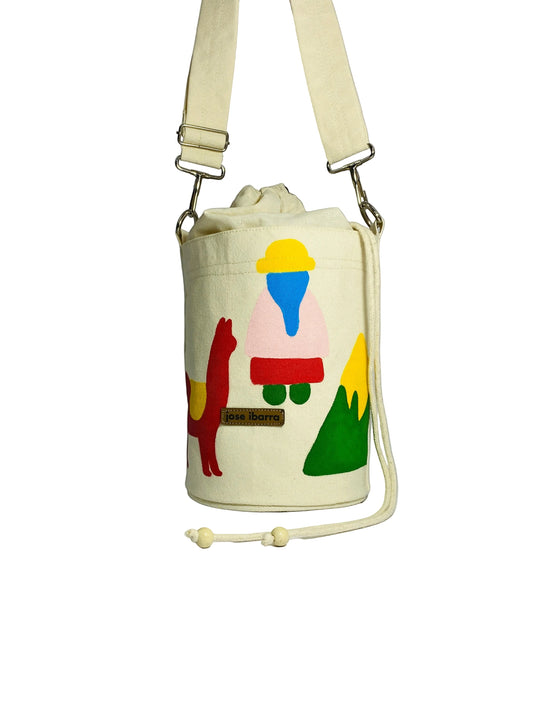 Jose Ibarra Estudio cream canvas bucket bag with hand-painted llama, figure, and mountain design. Adjustable strap.