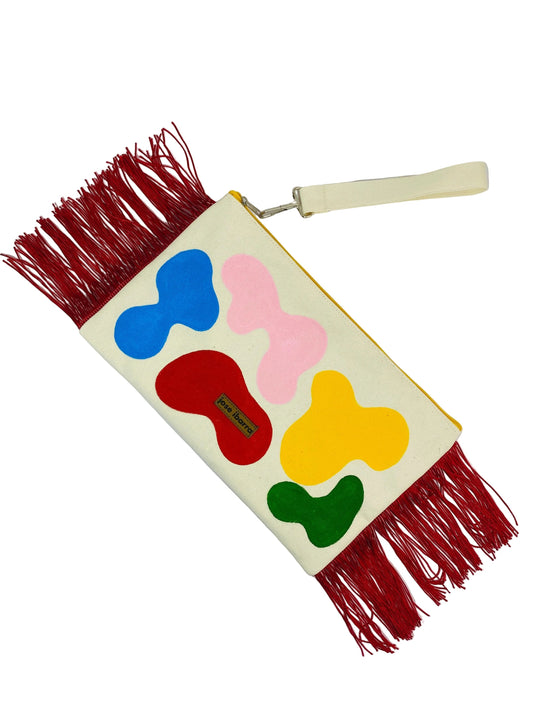 Jose Ibarra Estudio large cream cotton clutch with hand-painted abstract shapes in red, blue, pink, yellow, and green, and red fringe detail.