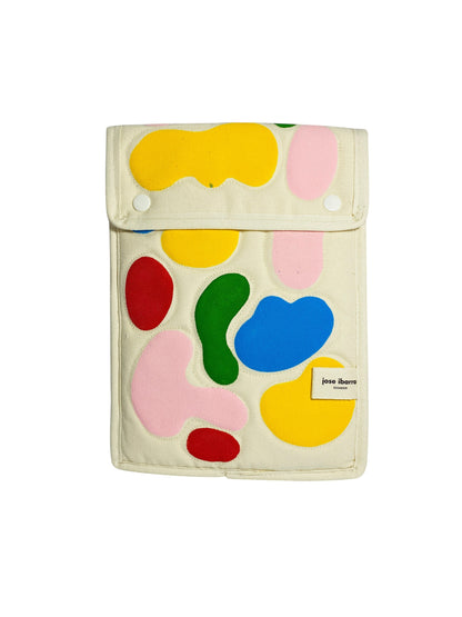 Jose Ibarra Estudio cream canvas iPad sleeve with colorful abstract appliqué shapes. Features a snap closure and internal lining.