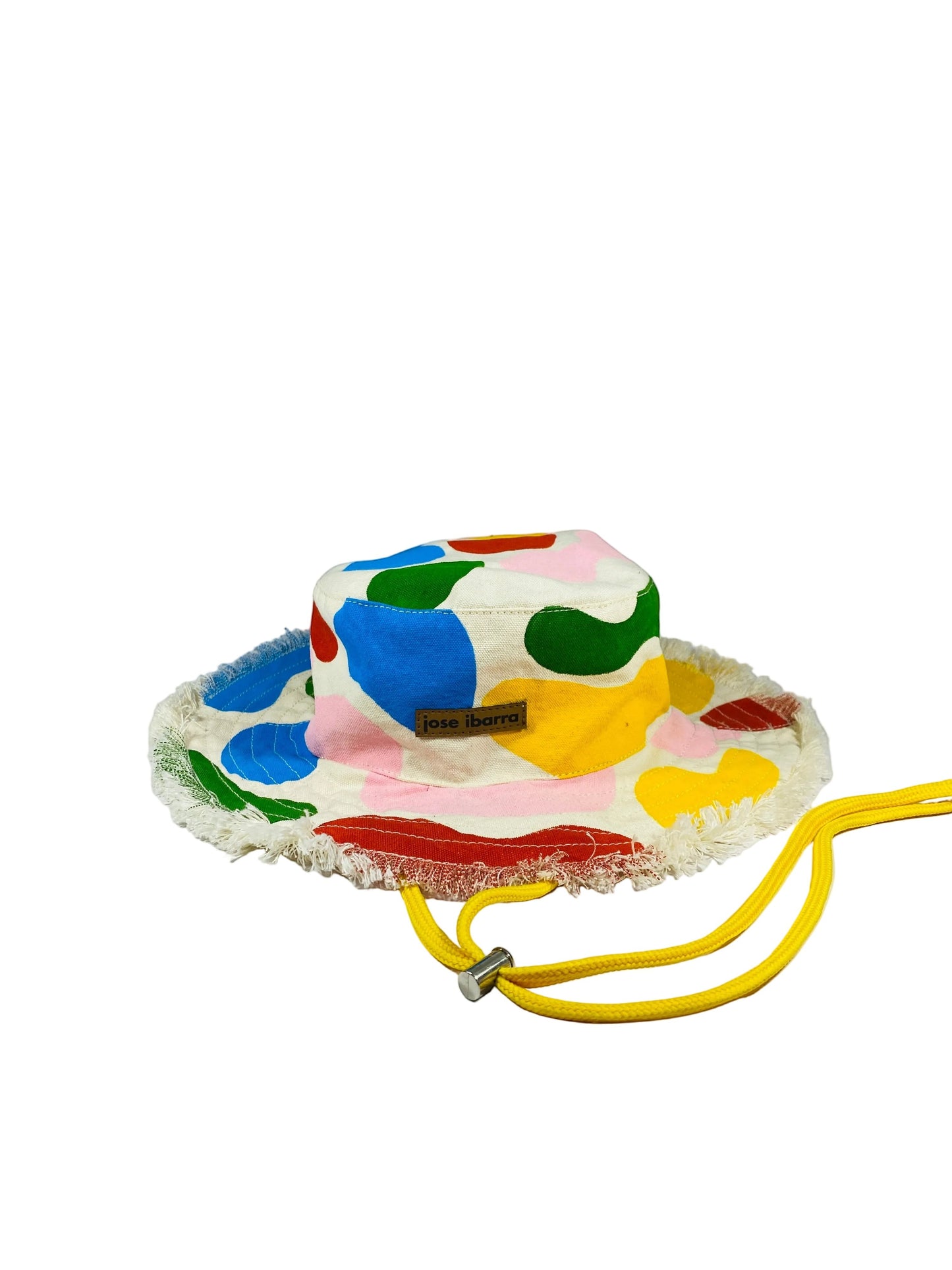 Jose Ibarra Estudio cream bucket hat with abstract colorful paint splatters, frayed brim, and yellow drawstring.