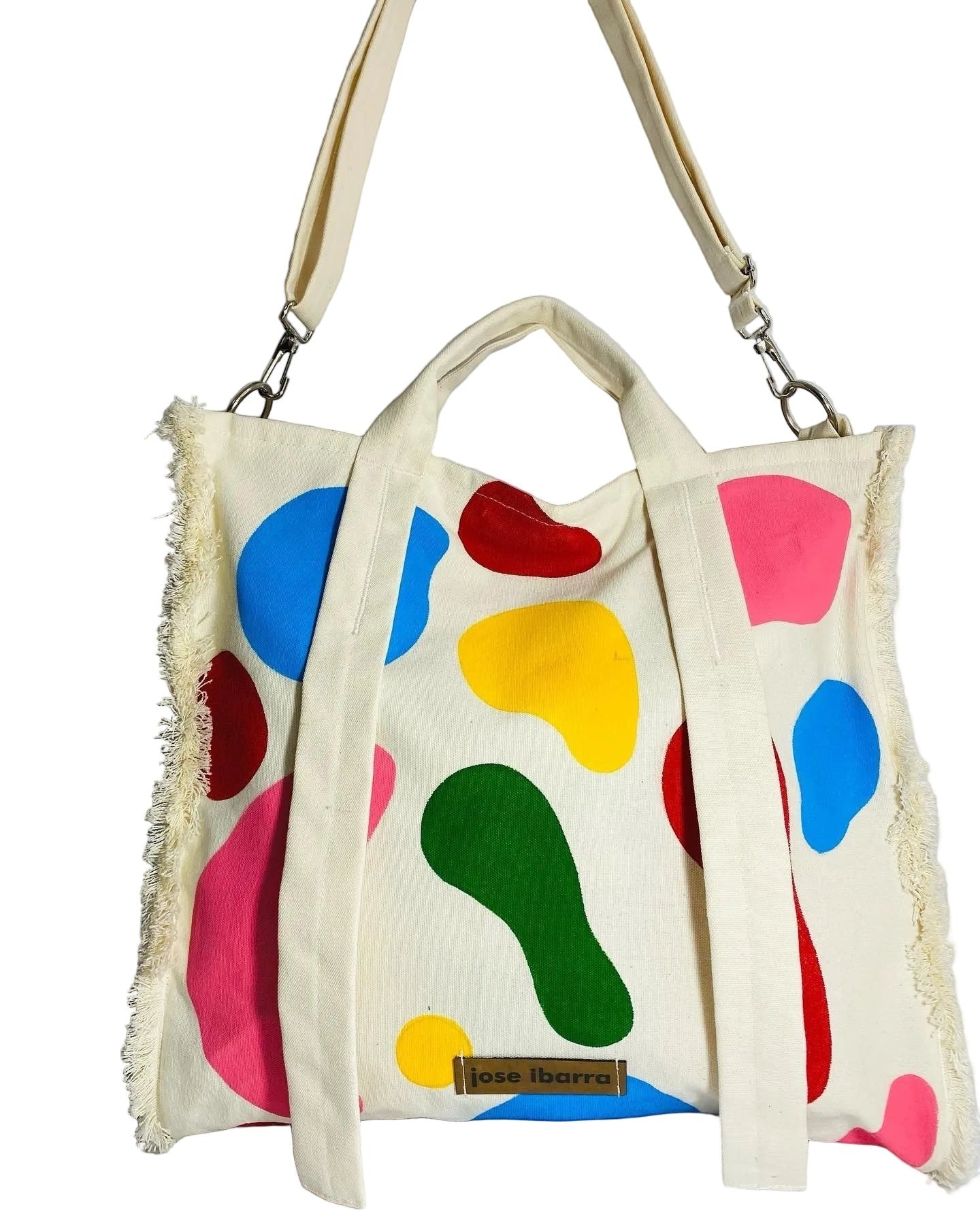 Jose Ibarra Estudio cream canvas tote bag with colorful abstract paint splatters and frayed edges. Includes shoulder strap.