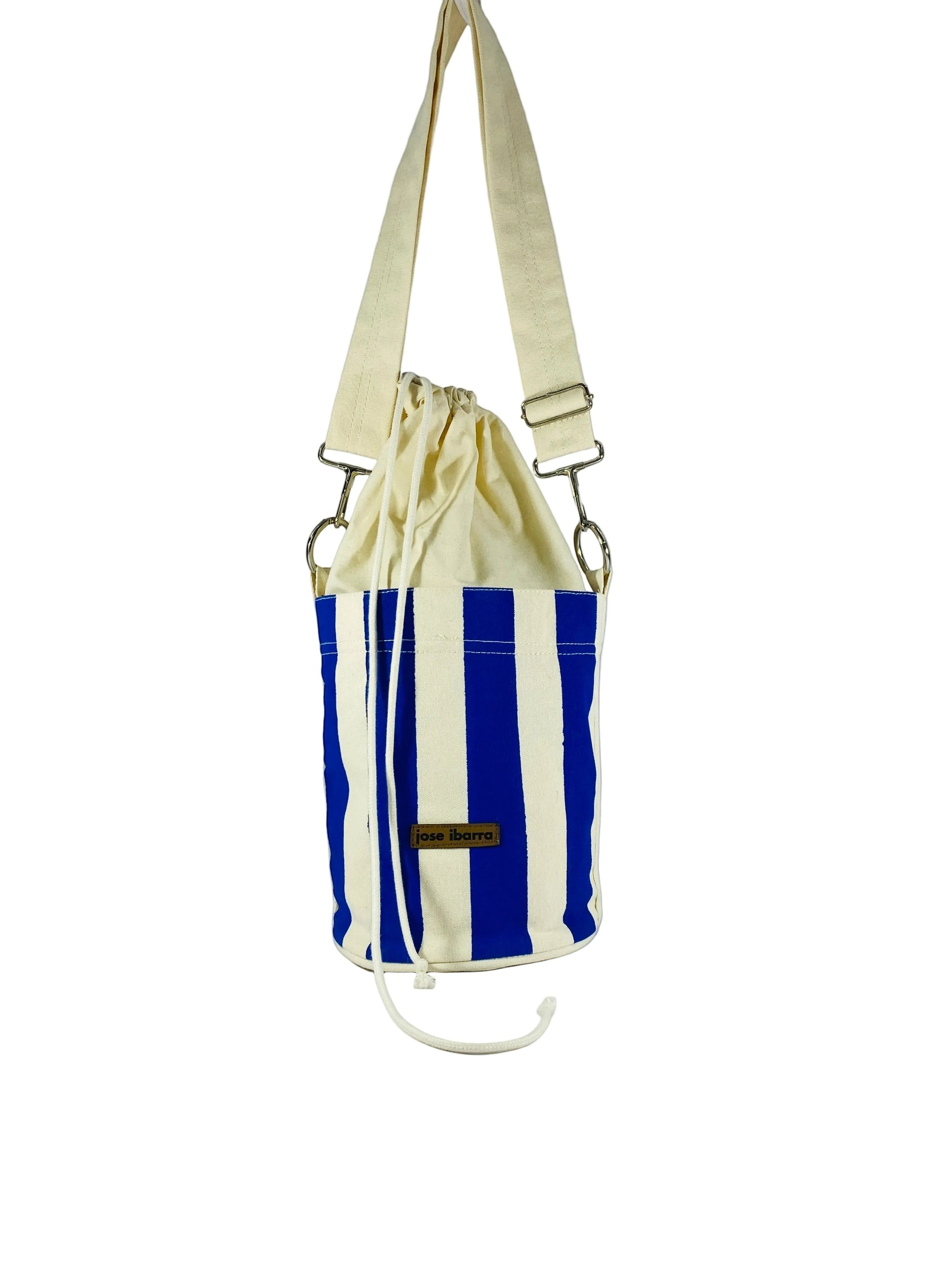 Jose Ibarra Estudio blue and white striped canvas bucket bag with drawstring closure and adjustable strap.