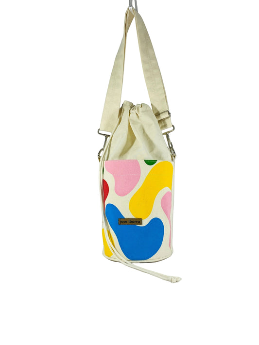 Jose Ibarra Estudio cream canvas bucket bag with abstract colourful hand-painted shapes and drawstring closure.