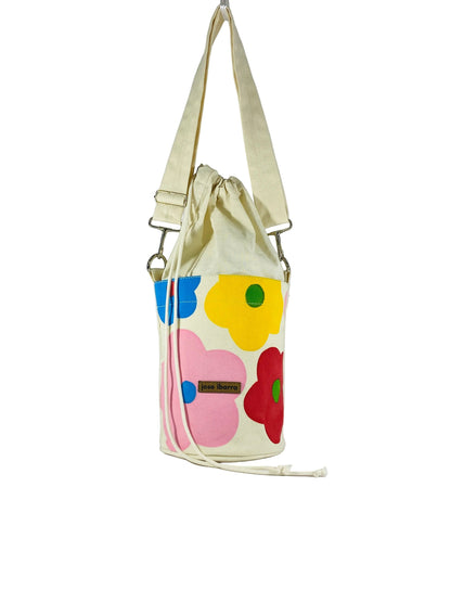 Jose Ibarra Estudio cream canvas bucket bag with hand-painted colorful floral appliques and drawstring closure.