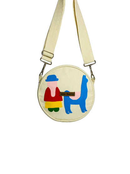 Jose Ibarra Estudio cream canvas round crossbody bag with hand-painted llama and person design, adjustable strap.