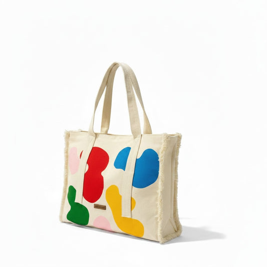Jose Ibarra Estudio cream canvas tote bag with abstract colorful shapes, frayed edges, and dual straps.