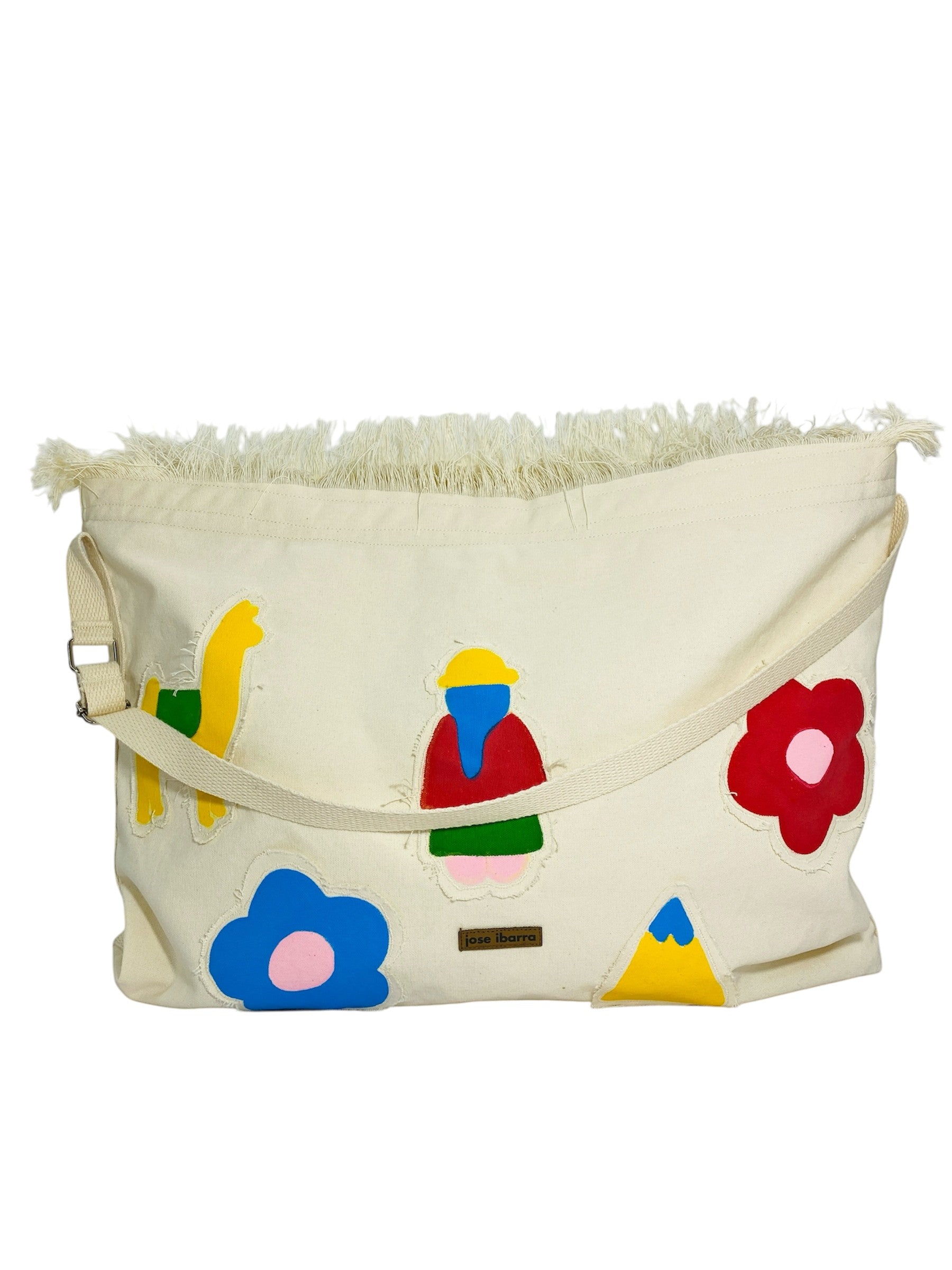 Jose Ibarra Estudio cream cotton canvas tote bag with colorful hand-painted appliqués of flowers, a llama, a figure, and mountains. Frayed top edge and adjustable strap.