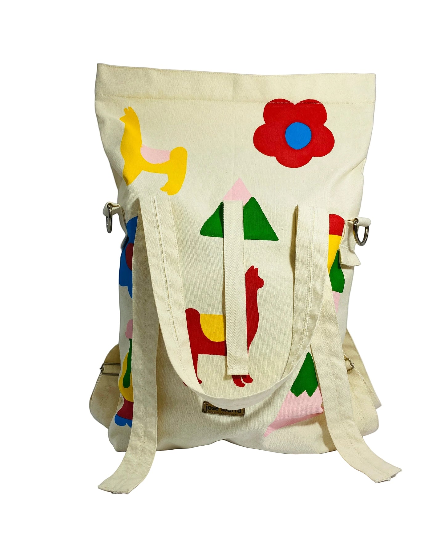 Jose Ibarra Estudio cream cotton canvas tote bag with hand-painted colorful llama, flower, and geometric designs. Convertible to backpack or crossbody.