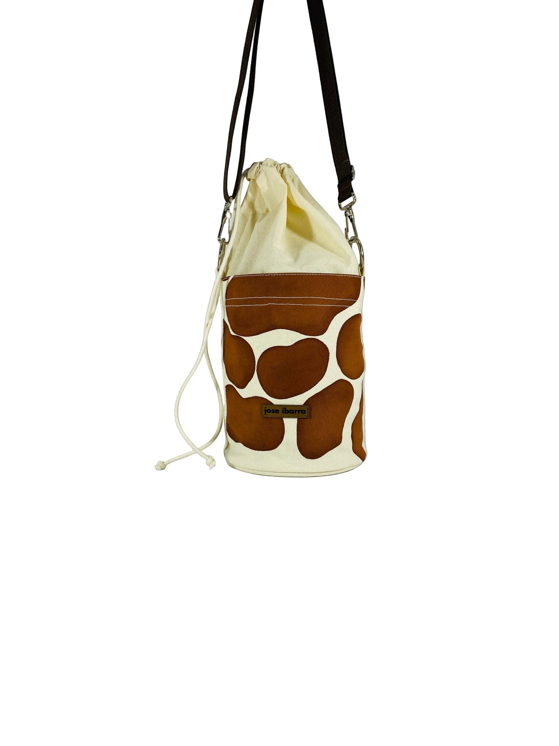 Jose Ibarra Estudio cream canvas bucket bag with brown cow print panels and drawstring closure.