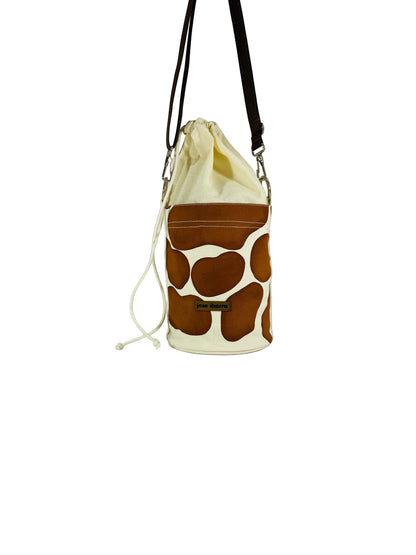 Jose Ibarra Estudio cream canvas bucket bag with brown cow print panels and drawstring closure.