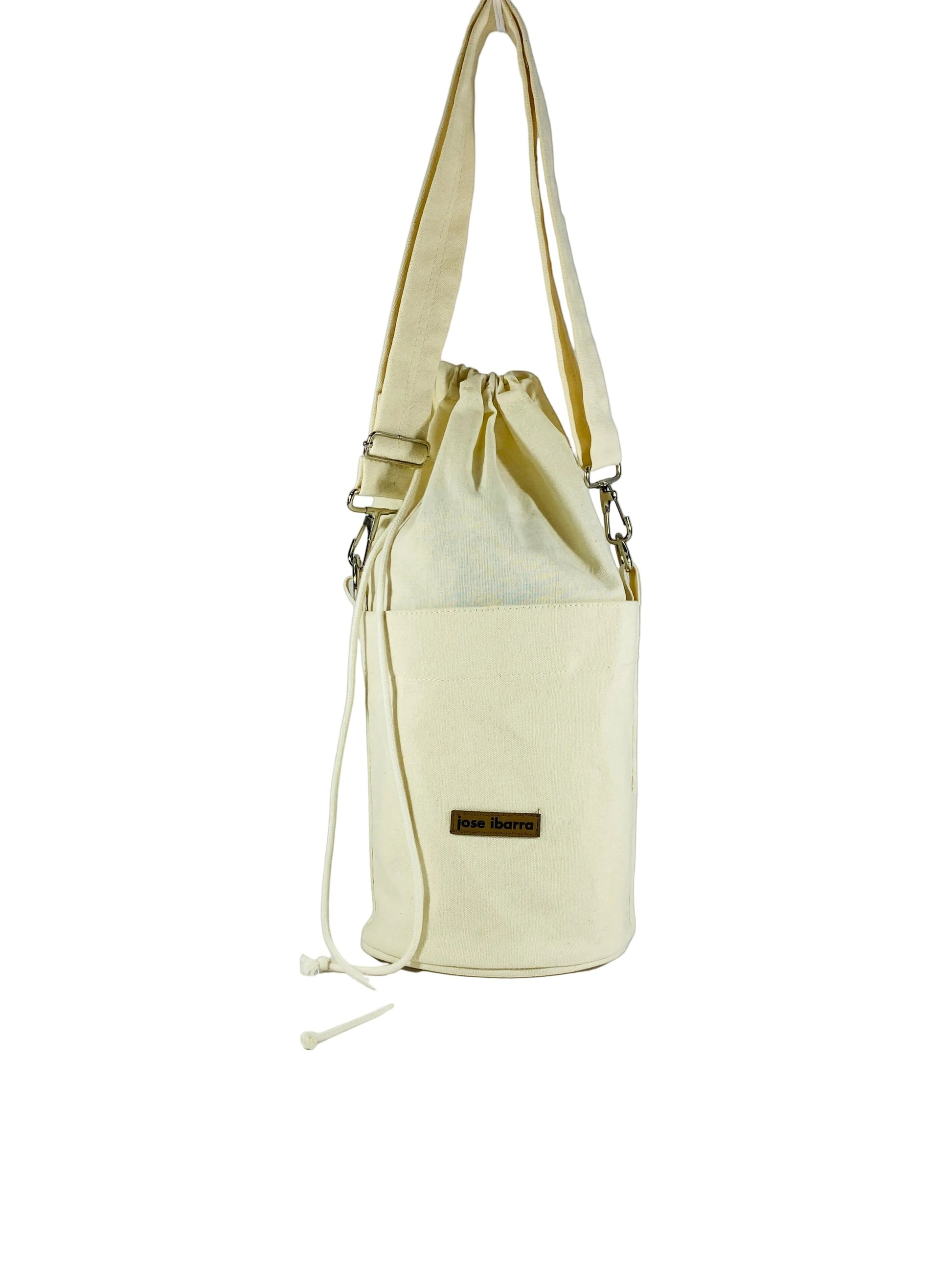 Jose Ibarra Estudio cream canvas bucket bag with drawstring closure and exterior pocket. Hand-painted details.