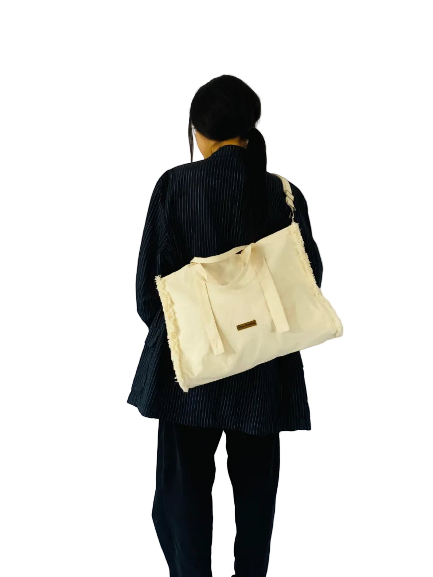 Jose Ibarra Estudio cream canvas tote bag with frayed edges and hand-painted details, includes strap. Model shown from back.