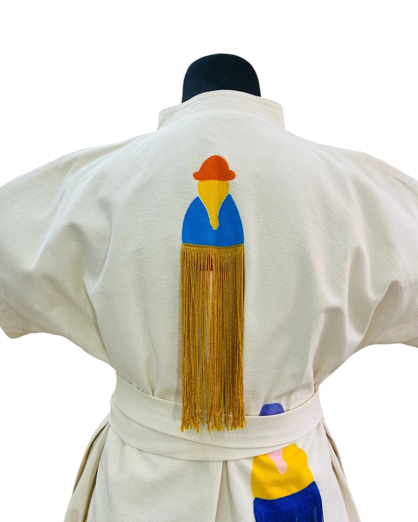 Jose Ibarra Estudio cream cotton dress with hand-painted Andean figure and fringe detail. Features a blue, yellow, and orange design with gold fringe.