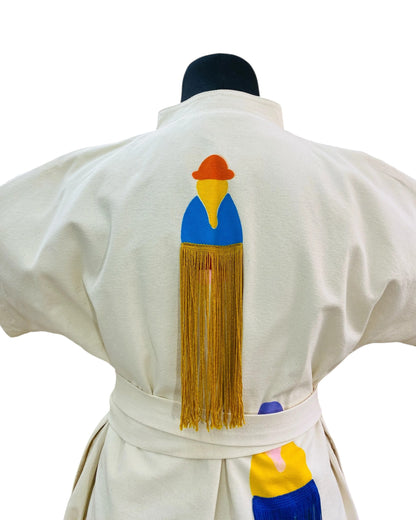 Jose Ibarra Estudio cream cotton dress with hand-painted Andean figure and fringe detail. Features a blue, yellow, and orange design with gold fringe.