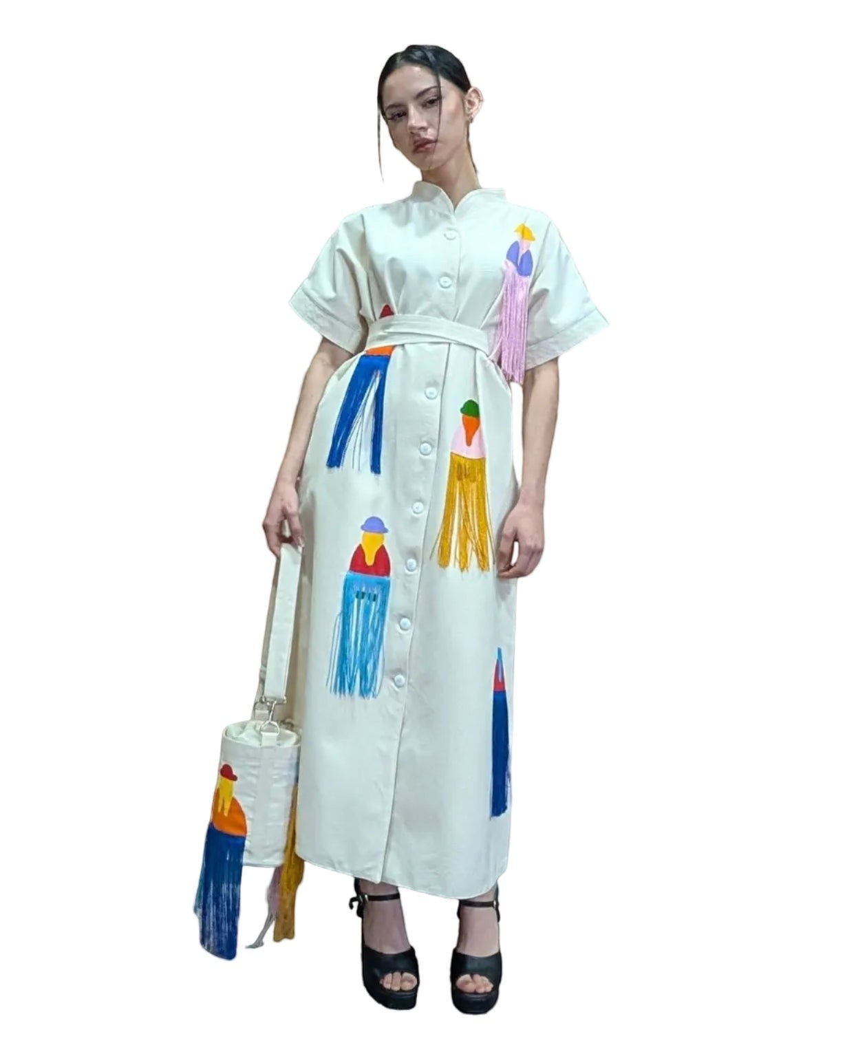 Jose Ibarra Estudio cream cotton dress with hand-painted Andean figures and colorful fringe details. Button-up front, belted waist, short sleeves.