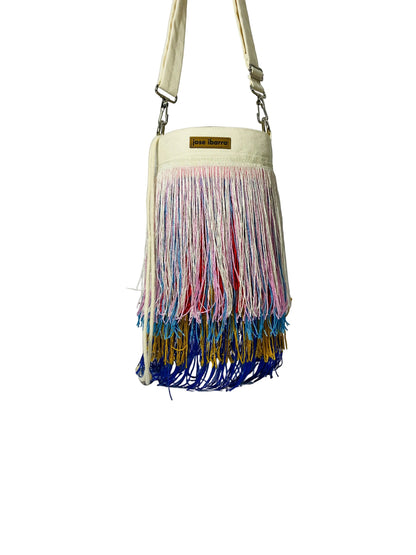 Jose Ibarra Estudio cream cotton bucket bag with multi-colored fringe detailing and adjustable strap.