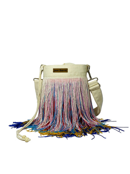 Jose Ibarra Estudio cream canvas bucket bag with multicolor fringe detailing and adjustable strap. Hand-painted, artisanal design.