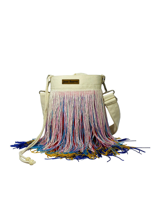 Jose Ibarra Estudio cream canvas bucket bag with multicolor fringe detailing and adjustable strap. Hand-painted, artisanal design.
