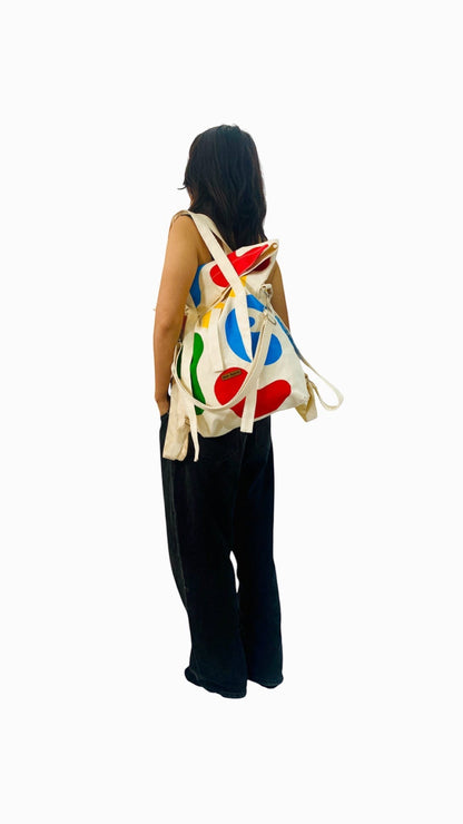 Jose Ibarra Estudio cream cotton tote backpack with hand-painted abstract red, blue, and green shapes. Versatile bag.