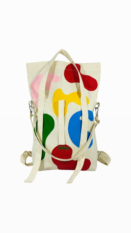Jose Ibarra Estudio cream cotton tote bag with hand-painted abstract colourful shapes in red, blue, green, yellow, and pink. Convertible to backpack or crossbody.