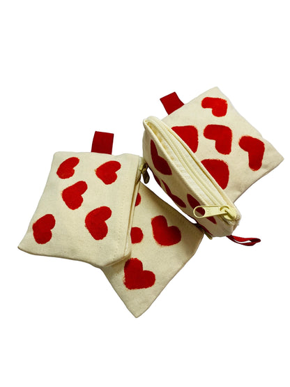 Jose Ibarra Estudio cream canvas coin purse with red hand-painted hearts, zipper closure, and red loop detail.