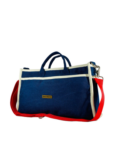 Jose Ibarra Estudio navy blue canvas tote bag with cream trim and red straps. Features dual handles, detachable shoulder strap, and internal pockets.