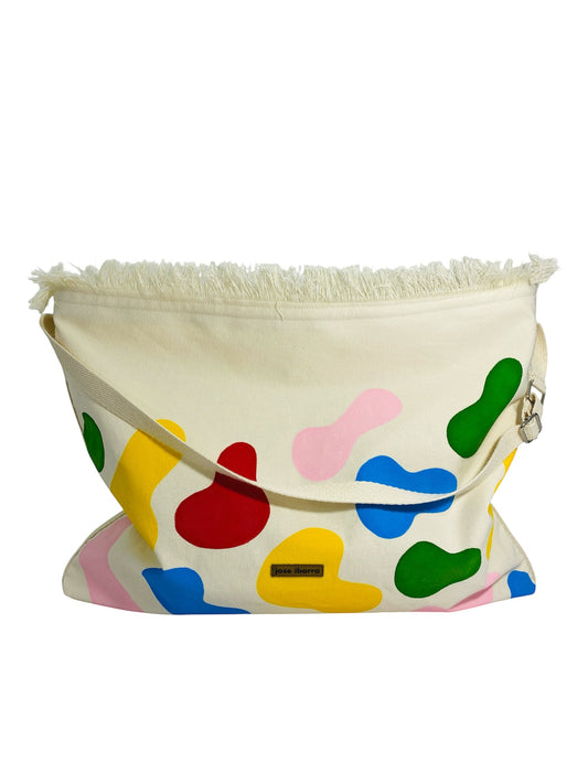 Jose Ibarra Estudio cream canvas tote bag with colorful abstract paint splatters and frayed top edge. Adjustable strap.