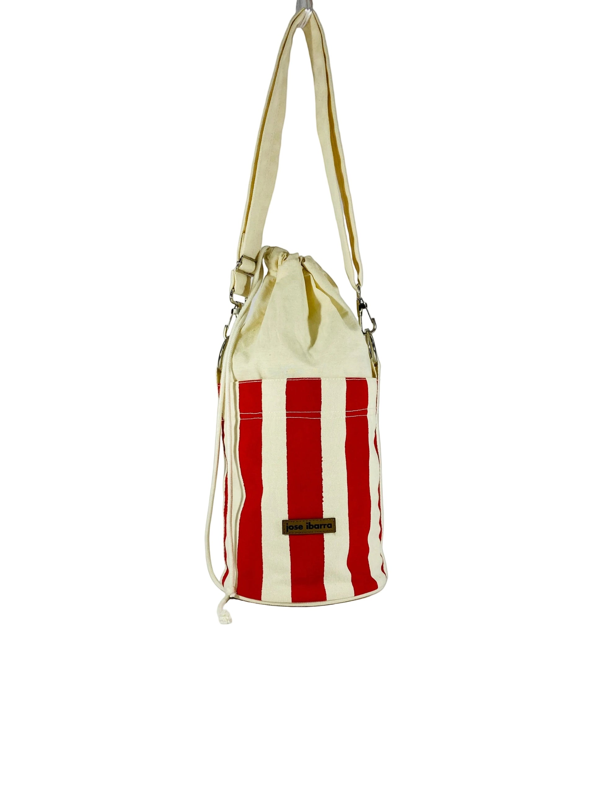 Jose Ibarra Estudio cream canvas bucket bag with red vertical stripes and drawstring closure. Hand-painted design.