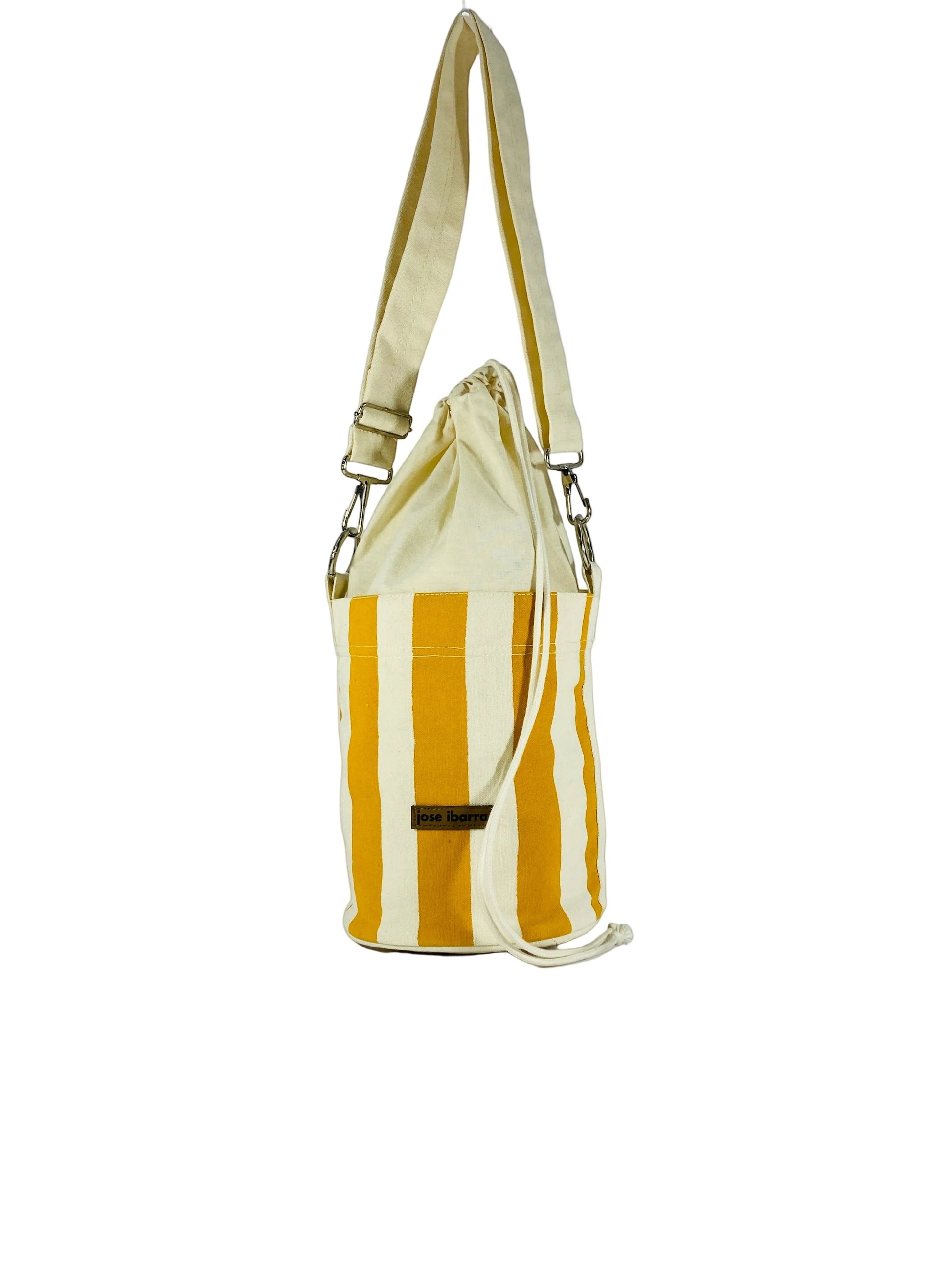 Jose Ibarra Estudio cream and mustard yellow striped canvas bucket bag with adjustable strap and drawstring closure.