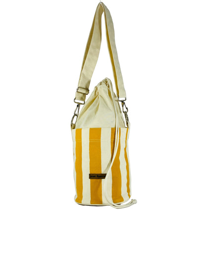 Jose Ibarra Estudio cream and mustard yellow striped canvas bucket bag with adjustable strap and drawstring closure.